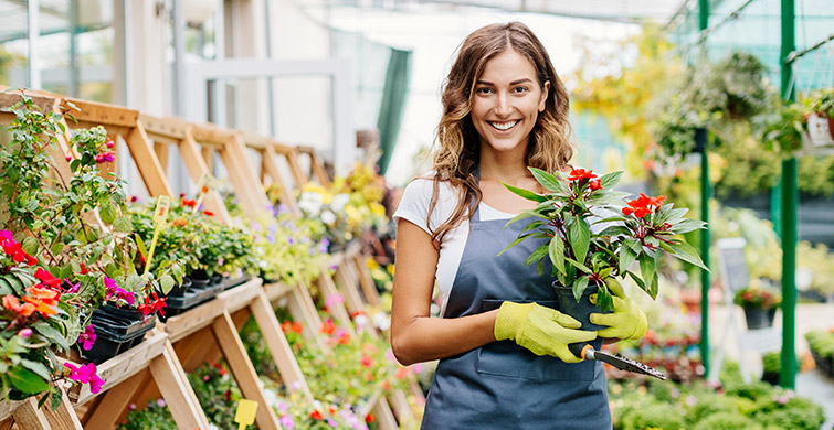 Woman in garden shop holding plant and spade
