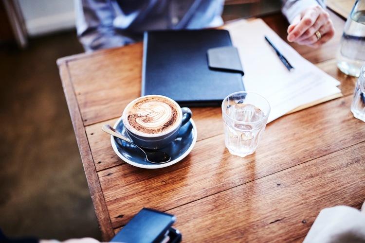 A coffee cup sits on a table with paperwork at a cafe.