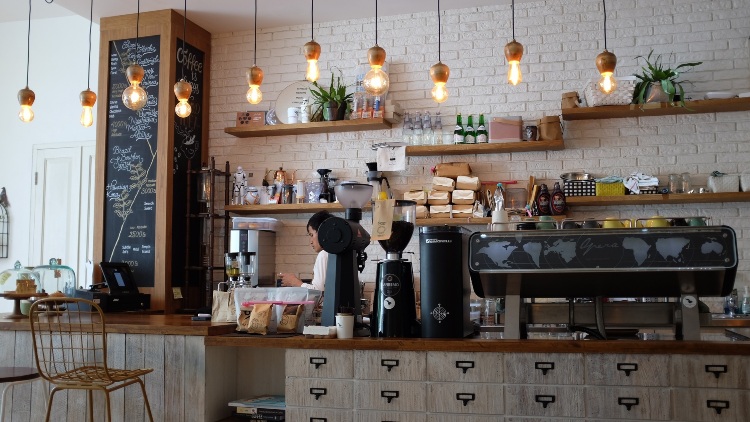 Server works behind a cluttered coffee counter in a cafe.