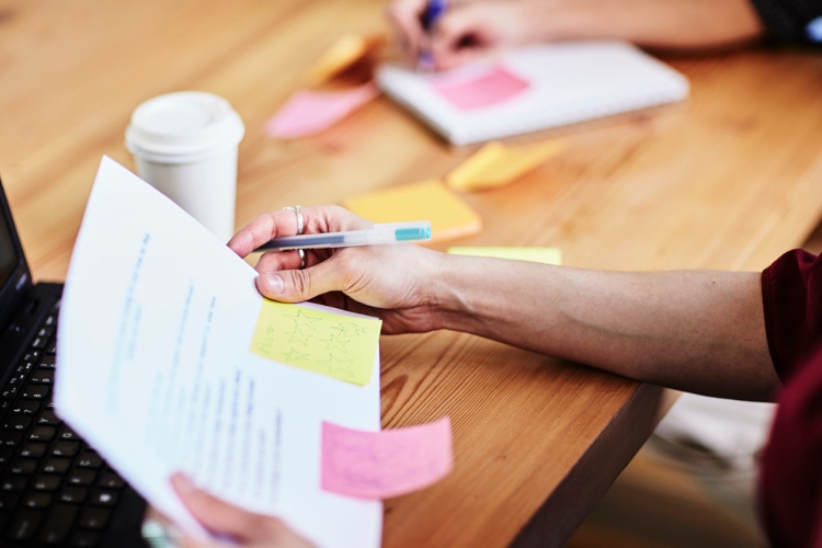 Someone holds a piece of paper with post-it notes attached, reviewing it.