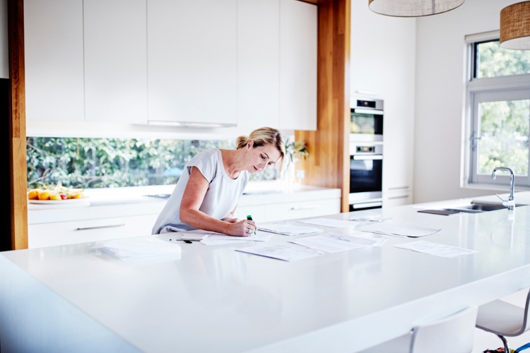 Woman highlights papers on a white benchtop.