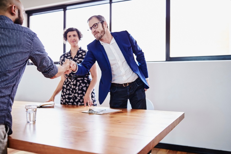 A man shakes another mans hand across a table.