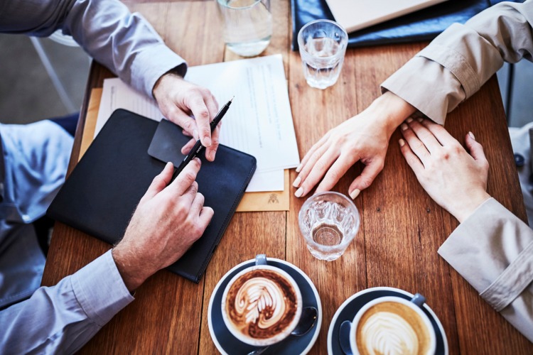 Hands on a table, with coffees, and paperwork.