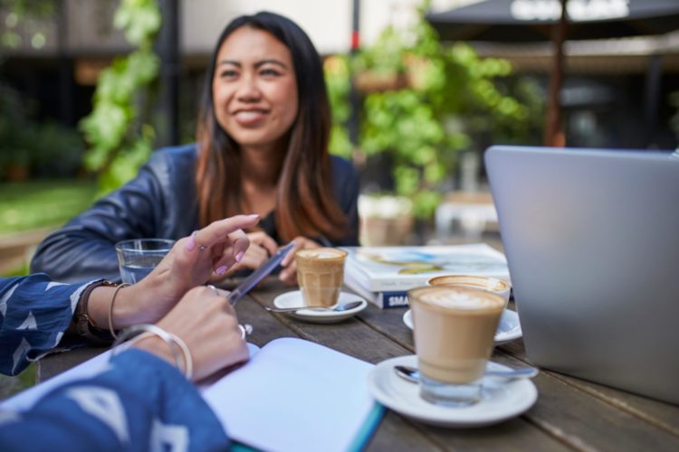 Two women drinking coffee at a table outside